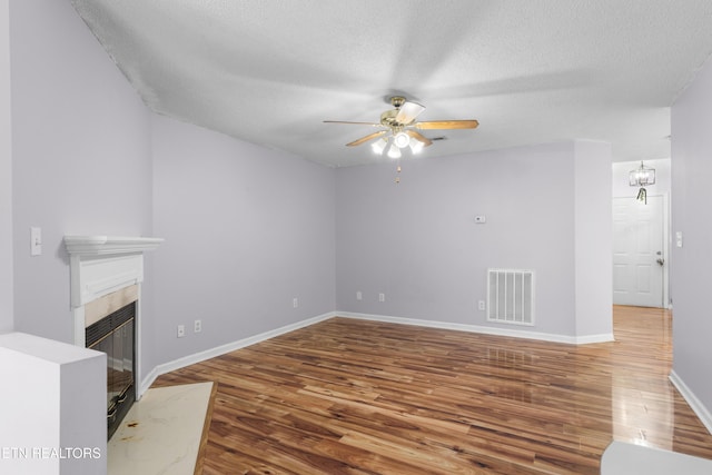 unfurnished living room with visible vents, ceiling fan with notable chandelier, a textured ceiling, wood finished floors, and a tile fireplace