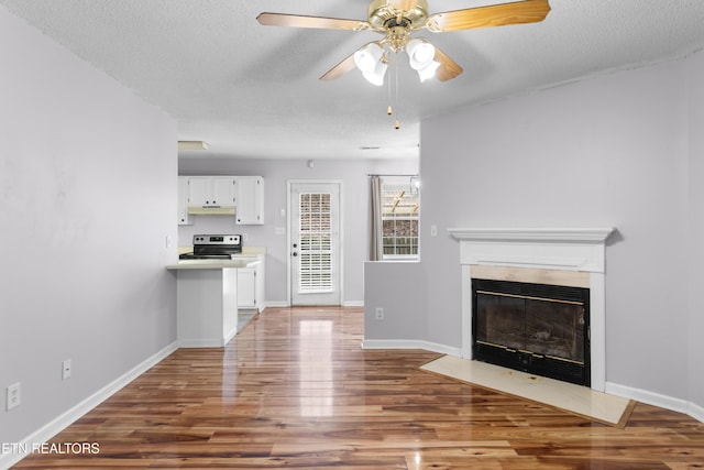 unfurnished living room with a fireplace with flush hearth, wood finished floors, baseboards, and a textured ceiling