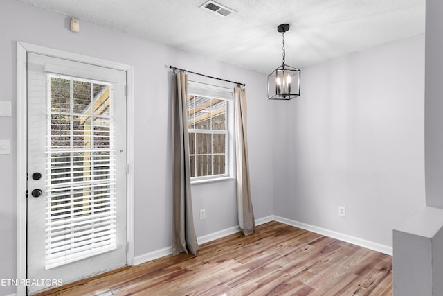 unfurnished dining area with visible vents, baseboards, light wood-style floors, a textured ceiling, and a chandelier