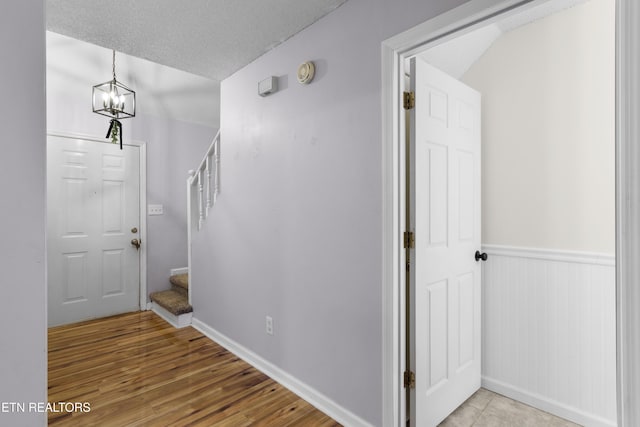 foyer entrance with a chandelier, stairway, a wainscoted wall, wood finished floors, and a textured ceiling