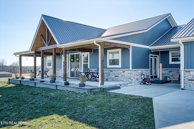 rear view of house with covered porch, stone siding, metal roof, and a yard