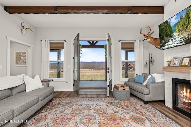 living area with wood finished floors, beam ceiling, and a glass covered fireplace