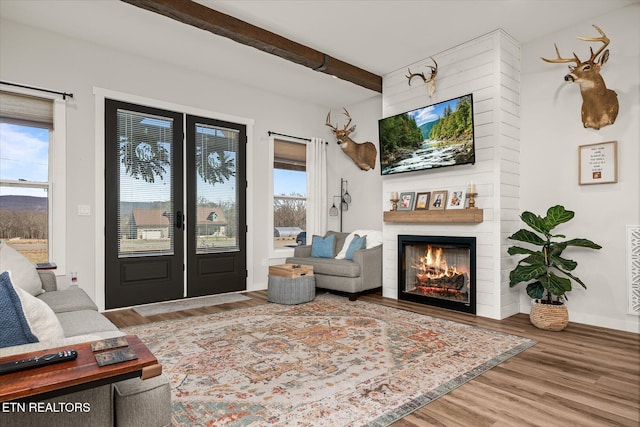 living room with a warm lit fireplace, wood finished floors, beam ceiling, and a healthy amount of sunlight