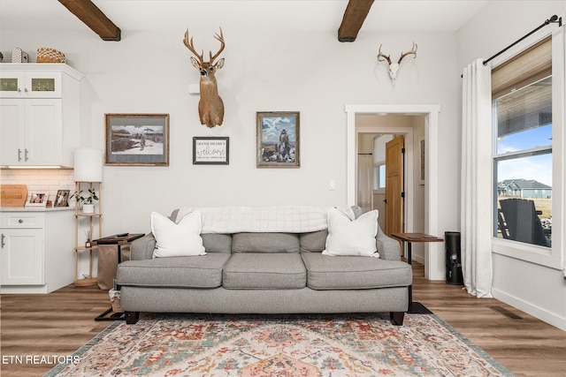 living room with beam ceiling, visible vents, baseboards, and wood finished floors