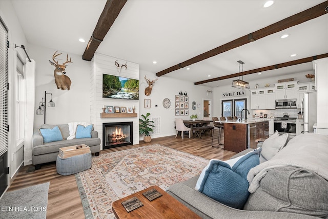 living room featuring recessed lighting, visible vents, light wood-style flooring, a large fireplace, and beamed ceiling