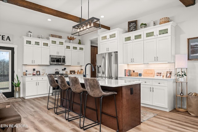 kitchen featuring stainless steel appliances, beamed ceiling, a sink, and light wood-style flooring