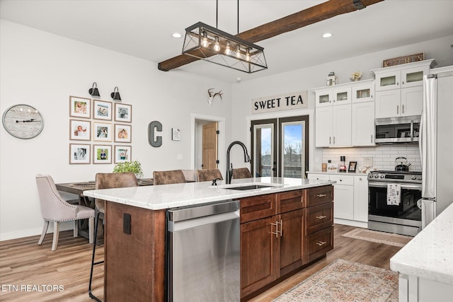 kitchen with stainless steel appliances, a sink, a kitchen breakfast bar, decorative backsplash, and a center island with sink