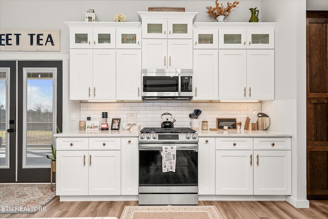 kitchen with stainless steel appliances, light wood-type flooring, backsplash, and white cabinetry