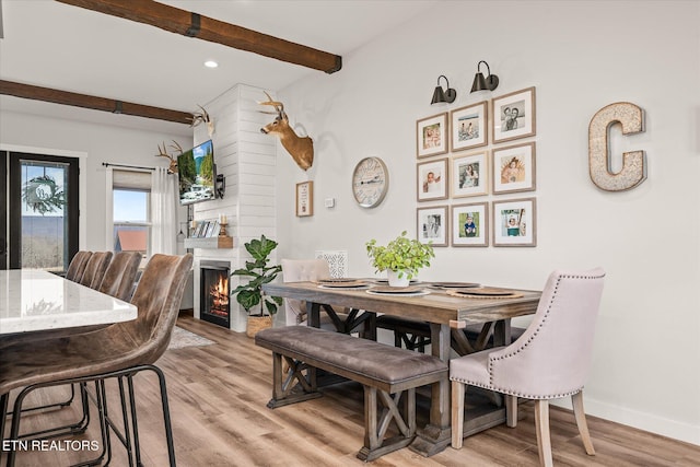 dining area featuring beam ceiling, a fireplace, light wood-style flooring, and baseboards