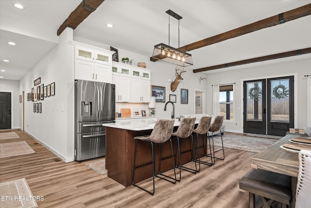 kitchen with stainless steel fridge with ice dispenser, light countertops, light wood-type flooring, decorative backsplash, and beamed ceiling