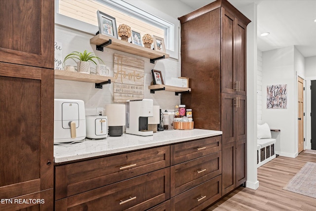 kitchen with light stone countertops, light wood-style floors, dark brown cabinetry, and open shelves