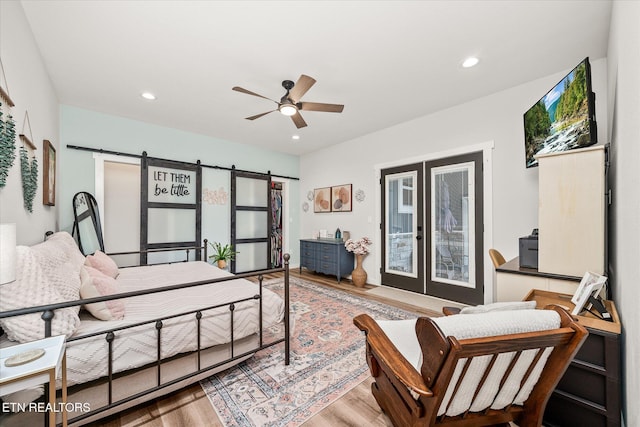 bedroom featuring recessed lighting, a barn door, wood finished floors, and french doors