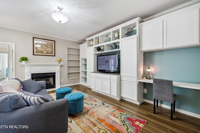 living area with dark wood-style flooring, a fireplace with flush hearth, baseboards, built in study area, and crown molding