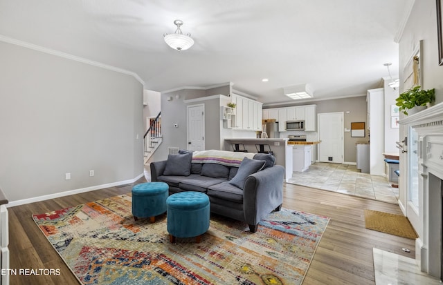 living area featuring baseboards, light wood-style flooring, a fireplace with flush hearth, stairs, and crown molding