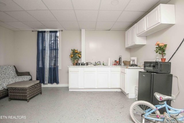 kitchen with black microwave, light countertops, a drop ceiling, and white cabinets