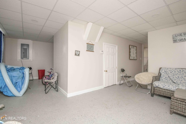 living area featuring a paneled ceiling, electric panel, baseboards, and speckled floor