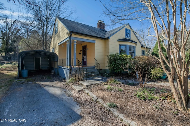 bungalow-style home featuring a chimney, aphalt driveway, roof with shingles, crawl space, and a detached carport