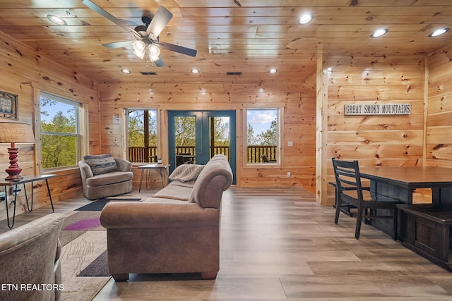 living room with french doors, wooden ceiling, light wood-style floors, and wooden walls