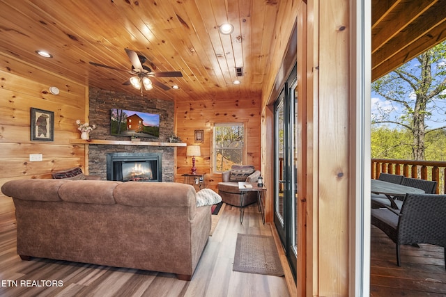 living area with a stone fireplace, wooden ceiling, wood finished floors, and wooden walls