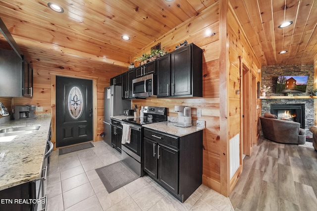 kitchen featuring stainless steel appliances, open floor plan, a sink, wood walls, and wooden ceiling