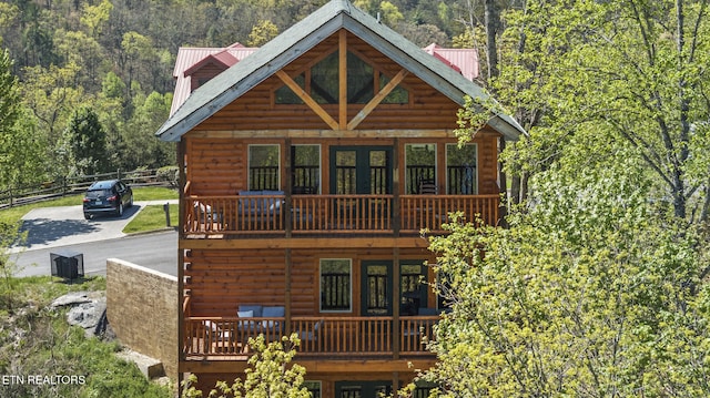 view of front of property with metal roof, a wooded view, a wooden deck, and fence