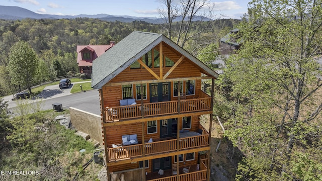 view of front of home with a balcony, a forest view, a mountain view, and roof with shingles