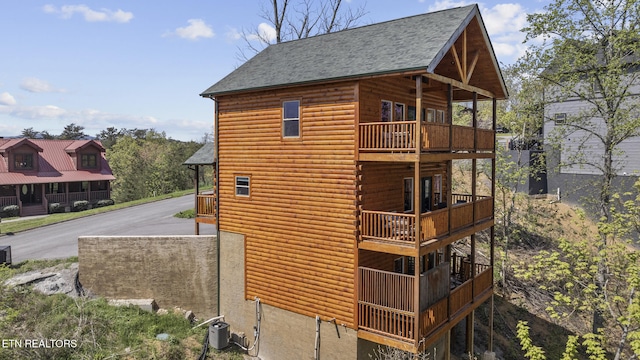 view of home's exterior featuring aphalt driveway, a shingled roof, a balcony, cooling unit, and faux log siding