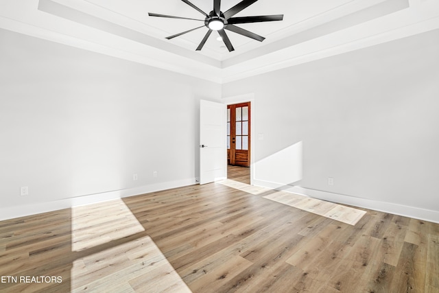 unfurnished room with a tray ceiling, wood finished floors, a ceiling fan, and baseboards