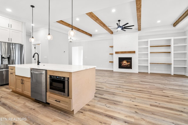 kitchen featuring appliances with stainless steel finishes, light wood-type flooring, beam ceiling, and a fireplace