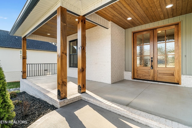 entrance to property featuring a porch, french doors, brick siding, and board and batten siding