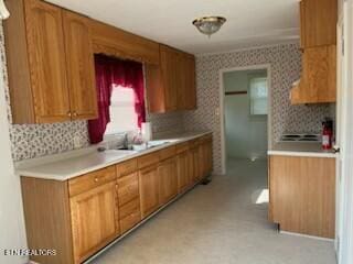 kitchen featuring brown cabinets, wallpapered walls, light countertops, and a sink