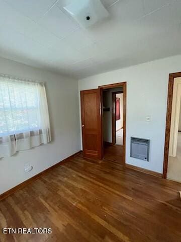 unfurnished bedroom featuring baseboards, dark wood-style flooring, and heating unit