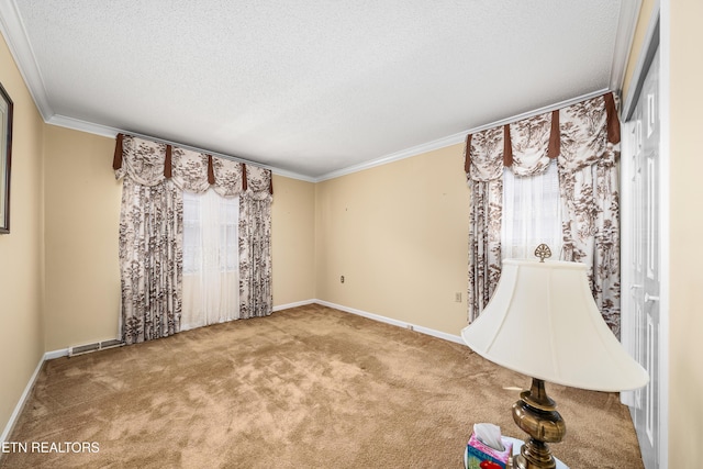 carpeted spare room with visible vents, baseboards, a textured ceiling, and ornamental molding