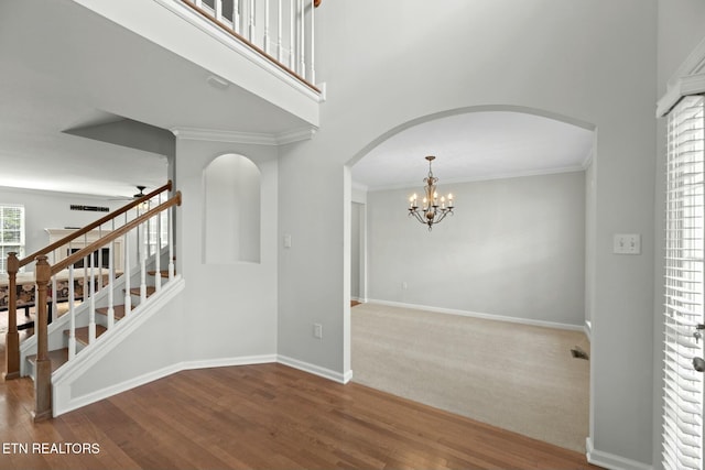 empty room with wood finished floors, baseboards, arched walkways, stairs, and a chandelier