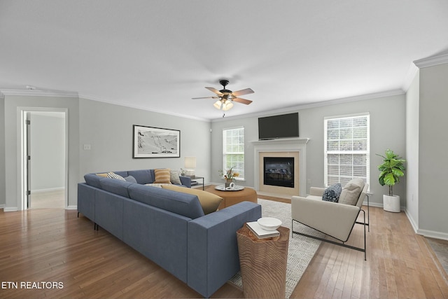 living room with a ceiling fan, baseboards, light wood finished floors, a fireplace with flush hearth, and ornamental molding