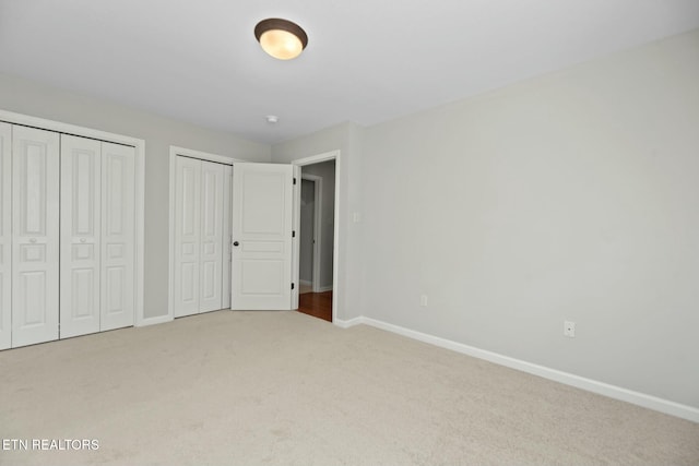 unfurnished bedroom with baseboards, multiple closets, and carpet floors