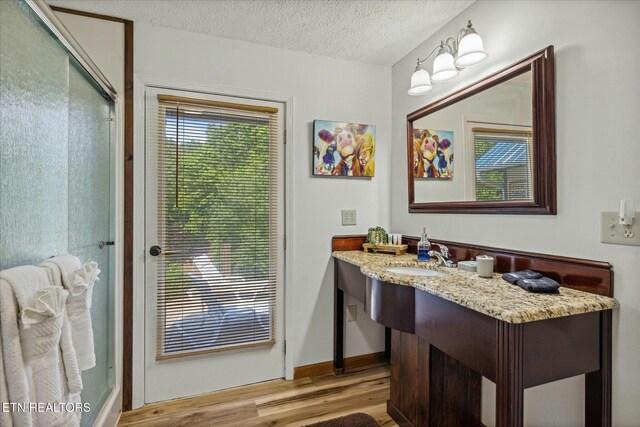 bathroom with a textured ceiling, a shower with shower door, wood finished floors, vanity, and baseboards