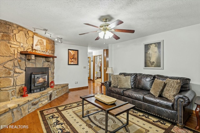 living area featuring a fireplace, a ceiling fan, a textured ceiling, wood finished floors, and baseboards