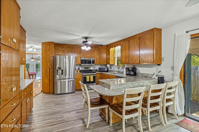 kitchen with brown cabinets, light wood finished floors, stainless steel appliances, a textured ceiling, and a peninsula