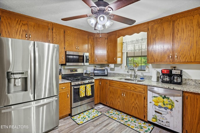 kitchen with light wood finished floors, light stone counters, appliances with stainless steel finishes, brown cabinets, and a sink