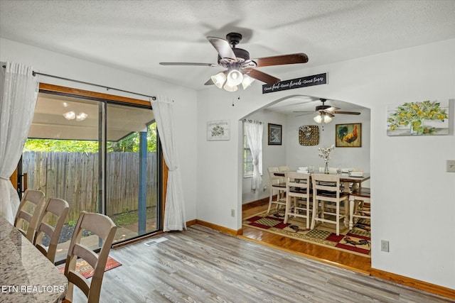 dining space featuring a textured ceiling, arched walkways, wood finished floors, and baseboards