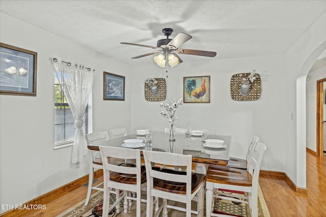 dining space with light wood-type flooring, arched walkways, a textured ceiling, and a ceiling fan