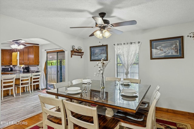 dining space featuring light wood finished floors, a textured ceiling, arched walkways, and a ceiling fan