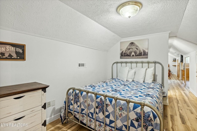 bedroom featuring lofted ceiling, visible vents, a textured ceiling, light wood-type flooring, and baseboards