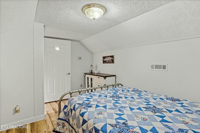 bedroom featuring light wood-style flooring, visible vents, vaulted ceiling, and a textured ceiling