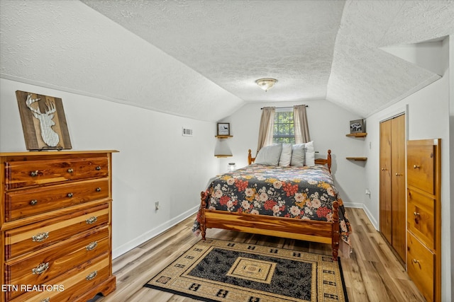 bedroom featuring light wood-type flooring, vaulted ceiling, a textured ceiling, and baseboards