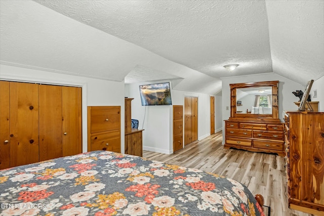 bedroom featuring lofted ceiling, light wood finished floors, and a textured ceiling