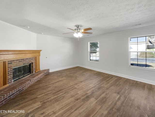 unfurnished living room with a brick fireplace, a textured ceiling, baseboards, and wood finished floors