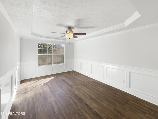 unfurnished room featuring a raised ceiling, wainscoting, ceiling fan, dark wood-type flooring, and a textured ceiling