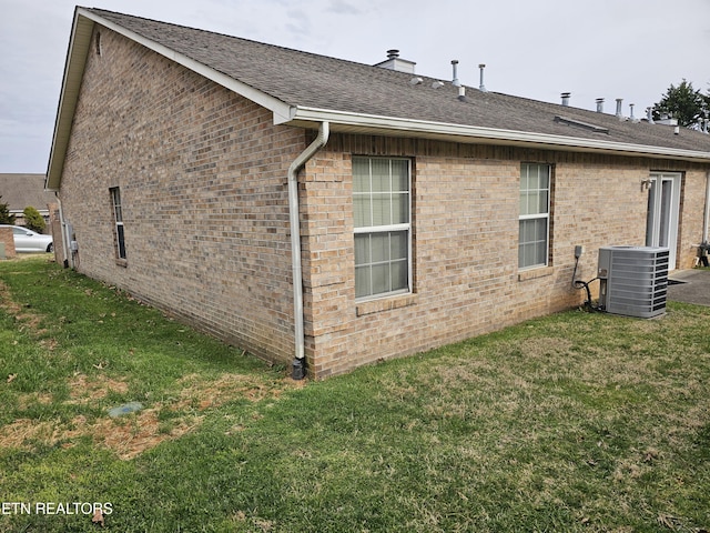 back of house with a shingled roof, central AC unit, a lawn, and brick siding